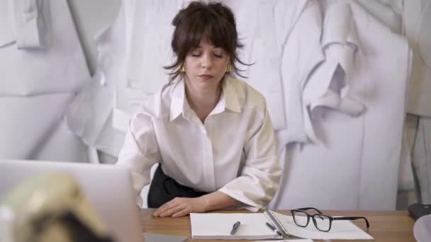 Diseñadora femenina está trabajando con el ordenador portátil en la mesa en el estudio de costura — Vídeos de Stock