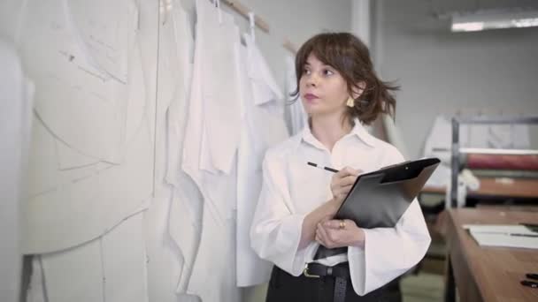 Diseñador de moda toma notas mientras mira los patrones en el estudio de costura — Vídeo de stock