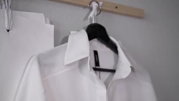 White shirt with black label on black hanger on wood rail rack hanger — Stock Video