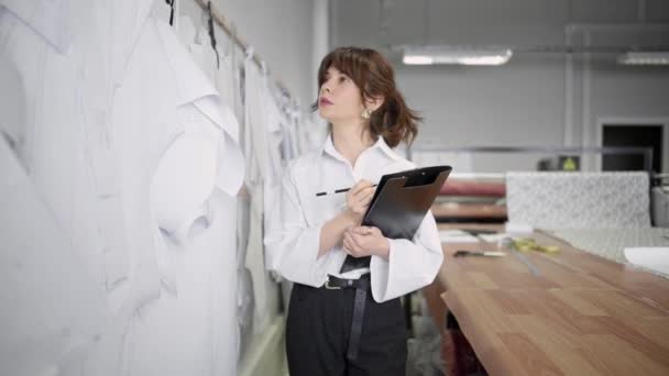 Diseñador de moda toma notas mientras mira los patrones en el estudio de costura — Vídeo de stock