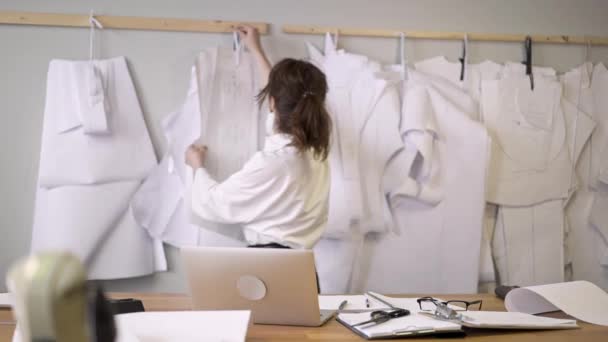 Модний дизайнер вибирає візерунки, що звисають до стіни в швейній студії — стокове відео
