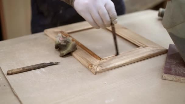 Мужские руки лакируют деревянную раму в мастерской по деревообработке — стоковое видео
