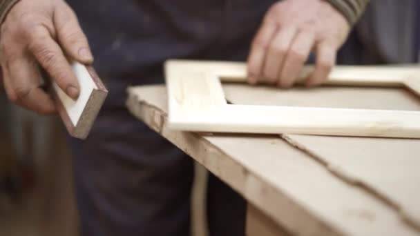Человек с наждачной бумагой на деревянной раме лежит на столе в мастерской — стоковое видео