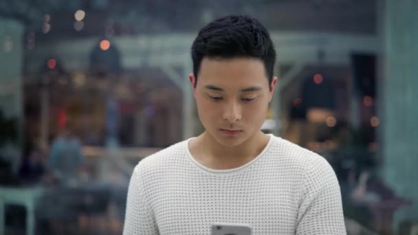 Plan du milieu de la marche masculine asiatique avec un téléphone sur fond de fenêtres — Video