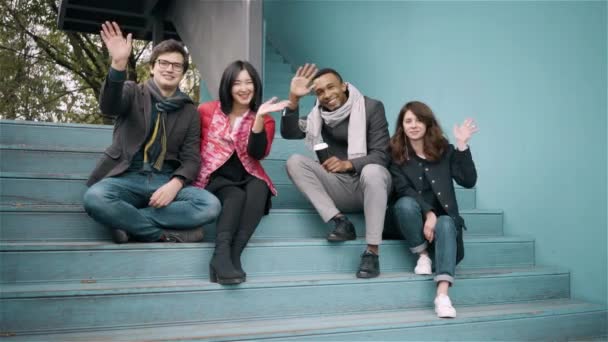 Разнообразная группа друзей, размахивающих руками, сидя на лестнице — стоковое видео