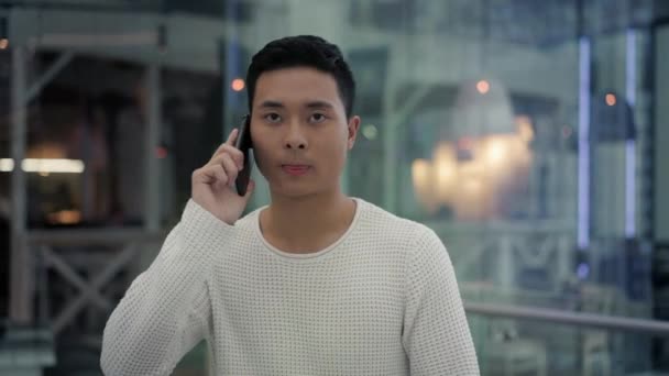 Повільний рух середній знімок азіатського чоловіка розмовляє по телефону під час ходьби — стокове відео