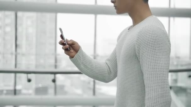 Средний снимок мужской ходьбы с телефоном на фоне окон — стоковое видео