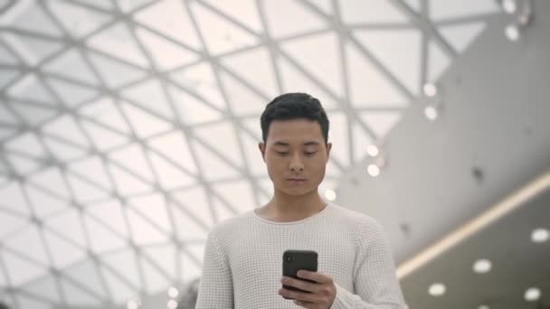 Zeitlupe mittlere Einstellung von asiatischen Mann zu Fuß mit einem Telefon an der Decke Hintergrund — Stockvideo