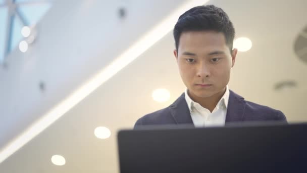 Pan shot van Aziatische mannelijke zakenman in pak werken met laptop op zijn knieën — Stockvideo