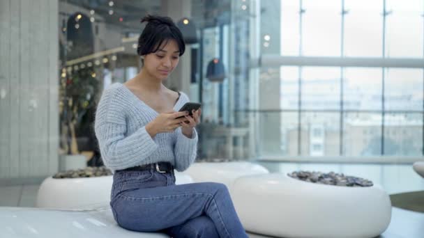 Midden schot van jonge Aziatische meisje texting zittend in rustzone van winkelcentrum — Stockvideo