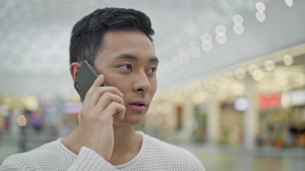 Primer plano de asiático macho hablando por teléfono en centro comercial fondo — Vídeo de stock