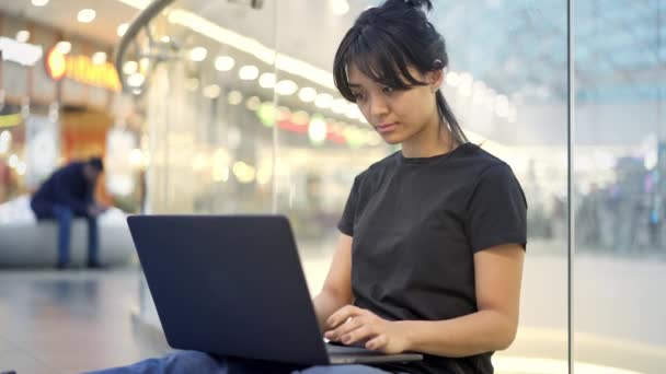 Azji młoda kobieta siedzi na podłodze z laptopem w centrum handlowym — Wideo stockowe