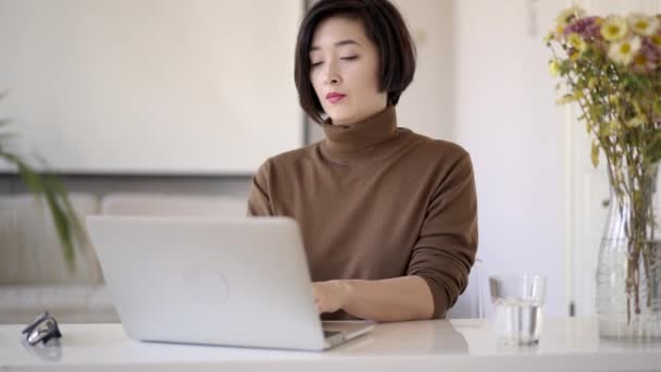Азиатская женщина короткая стрижка работает с ноутбуком в белом домашнем офисе — стоковое видео