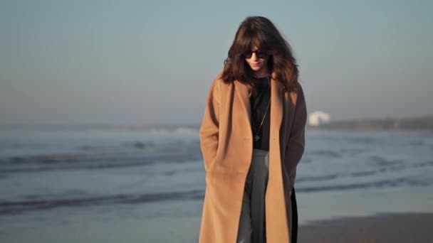 Медленное движение молодой женщины в пальто на фоне океанских волн — стоковое видео