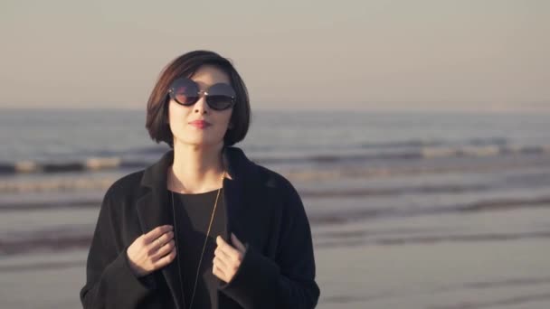 Медленное движение азиатской женщины в пальто на фоне океанских волн — стоковое видео