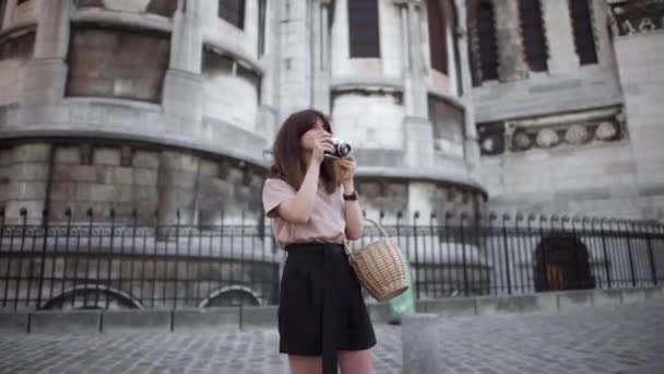 Bella giovane donna dai capelli scuri, vestita con pantaloncini neri e una t-shirt beige, fotografa la città. Ritratto in tempo reale da destra a sinistra . — Video Stock