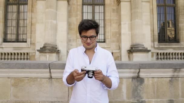 PARÍS, FRANCIA, ABRIL 2019. Hombre joven en camisa blanca haciendo foto con una cámara de cine en el fondo del museo del Louvre — Vídeos de Stock