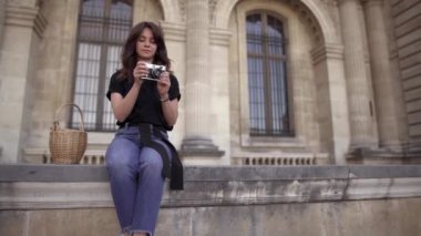 Koyu saçlı, kot pantolon ve siyah tişört giyen genç kadın şehrin fotoğraflarını çekiyor. Sağdan sola pan gerçek zamanlı geniş çekim.