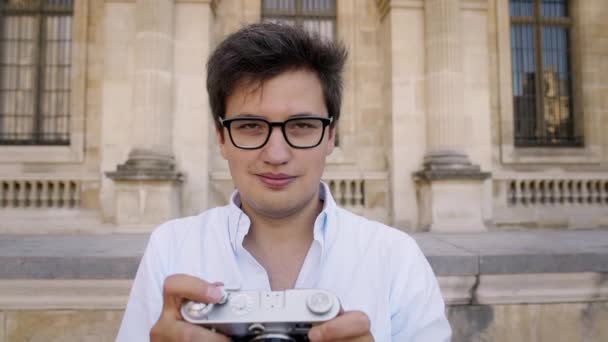 PARIS, FRANCE, APRIL 2019. Young man in white shirt making photo with a film camera on background of Louvre museum — Stock Video