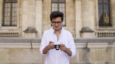 Paris, Fransa, Nisan 2019. Beyaz gömlekli genç adam Louvre Müzesi'nin arka planında bir film kamera ile fotoğraf yapma
