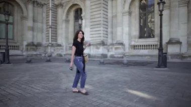 Koyu saçlı, kot pantolon ve siyah tişört giymiş güzel bir genç kadın, Paris'i dolaşıyor. Gerçek zamanlı geniş atış.