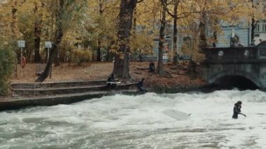 Münih, Almanya, 18 Kasım 2019: Eisbach nehri üzerinde bir dalga urban surfers gerçek zamanlı çekim. Münih English Garden'da Nehir Sörfü, Münih, Almanya.