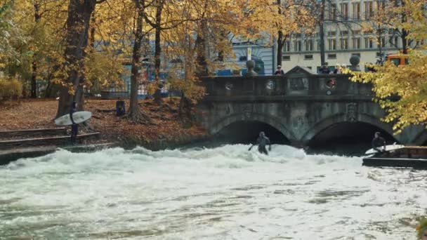 Мюнхен, Німеччина, 18 листопада 2019: в режимі реального часу широкий постріл міських серферів на хвилі на річці Айзенбах. Річковий серфінг в англійському саду Munichs, Мюнхен, Німеччина — стокове відео