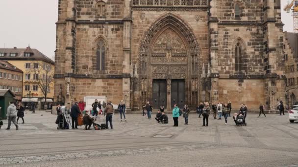 NUREMBERG, ALEMANIA - 30 de noviembre de 2019: Foto en tiempo real de personas caminando por la plaza y escuchando a músicos callejeros en el fondo de la iglesia de St. Lorenz, Nuremberg, Alemania . — Vídeo de stock