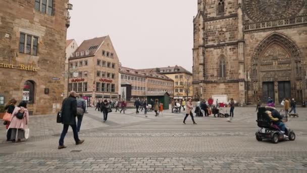 ニュルンベルク、ドイツ - 2019年11月30日:セントローレンツ教会、ニュルンベルク、ドイツの背景に広場を歩く人々のショットを確立する左から右のパンリアルタイム. — ストック動画
