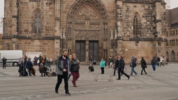 NUREMBERG, ALEMANIA - 30 de noviembre de 2019: plano medio en tiempo real de personas caminando por la plaza y escuchando a músicos callejeros en el fondo de la iglesia de St. Lorenz, Nuremberg, Alemania . — Vídeos de Stock