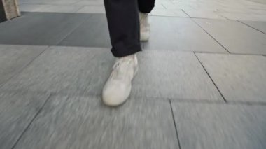 Beyaz adam spor ayakkabılarının yerden görünüşü kaldırım boyunca yürüyor.