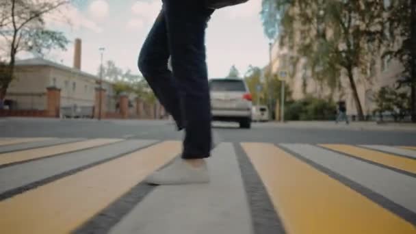 Jovem de calças azuis e tênis brancos está atravessando a estrada — Vídeo de Stock
