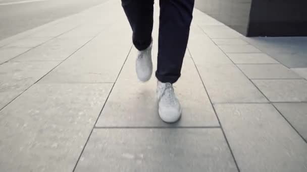 Utsikt från marknivå av vita sneakers långsamt promenader längs trottoaren — Stockvideo