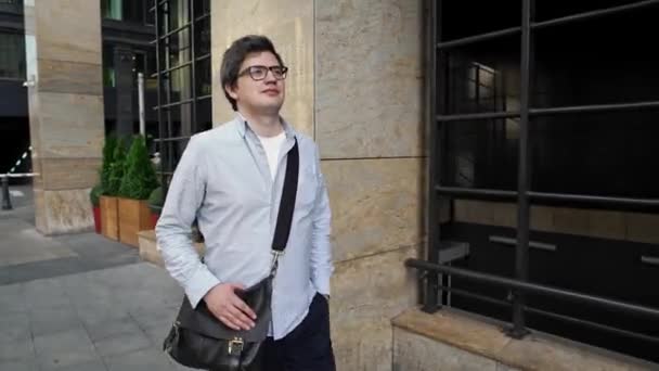 Man in eyeglasses walking along the street with a shoulder bag — Stock Video