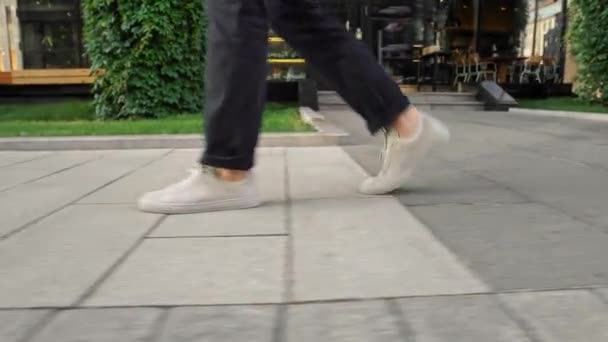 Profile view from ground level of white men sneakers walking along pavement — ストック動画