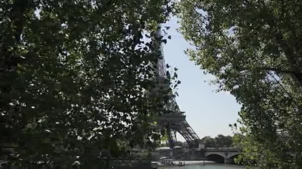 Roll shot wieży Eiffla pojawiające się z zielonych drzew na tle błękitnego nieba — Wideo stockowe