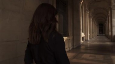 Siyah elbiseli kadın Louvre Müzesi 'nin önünde fotoğraf çekmek için dönüyor.