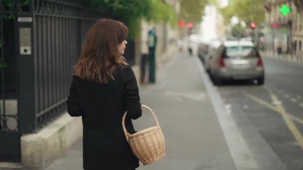 Slow motion back view van de vrouw op straat wandelen met een rieten mand — Stockvideo