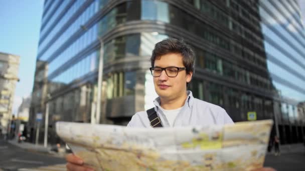 Pan shot of man with map standing in the center of the roading looking at the buildings — Stockvideo