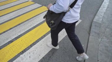 Mavi pantolonlu ve beyaz ayakkabılı adam karşıdan karşıya geçiyor.