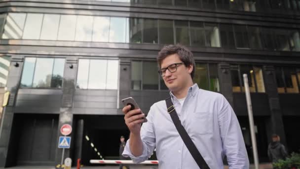 Plan panoramique de l'homme avec un smartphone sur fond de centre d'affaires en verre — Video