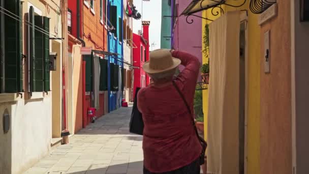 Burano adasında renkli evlerin fotoğraflarını çeken bir kadın. Burano adası parlak boyalı evleriyle ünlüdür. — Stok video