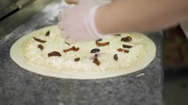 Peynirli pizzanın üzerine siyah zeytin koyarak elde yapılan bir aşçı pozu.