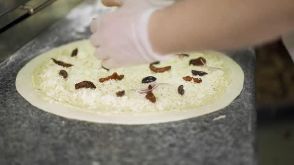 Handheld shot of cook putting black olives on cheese pizza raw dough — Stock Video