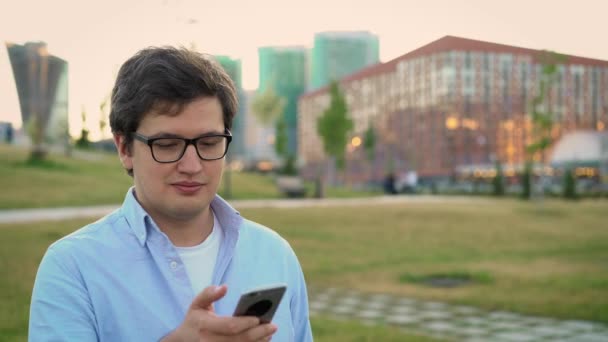 Портрет взрослого мужчины с помощью мобильного телефона на фоне газона в парке — стоковое видео