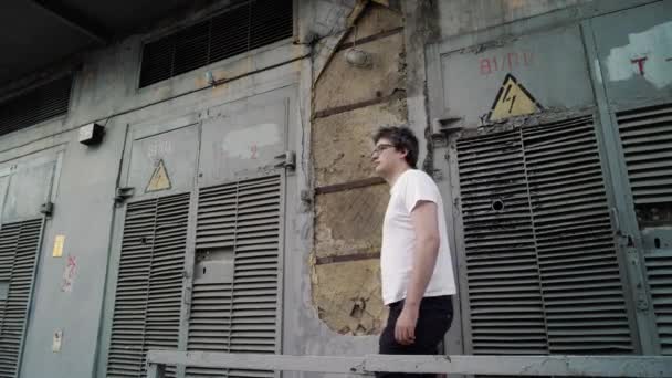 Взрослый мужчина стоит на фоне серых старых дверей высокого напряжения — стоковое видео