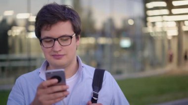 Dışarıda cep telefonuyla yazı yazan genç bir adamın ön manzara portresi.