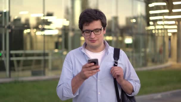 Vista frontal plano medio de hombre joven escribiendo en el teléfono celular al aire libre — Vídeo de stock