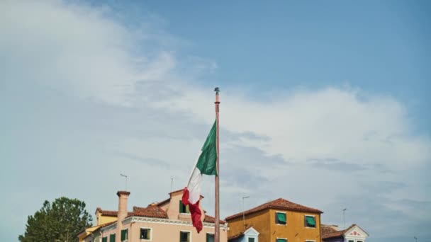 Italian flag waving in the wind with a blue sky and houses in the background. Real time shot — Stock Video