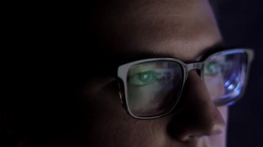 Gece geç saatte gözlüklü bir adam dizüstü bilgisayarın önünde kayıyor.